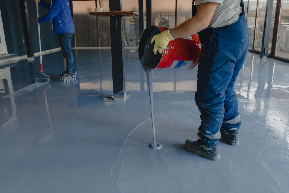 A man is engaged in painting a room blue, representing epoxy flooring services in Renton, WA.