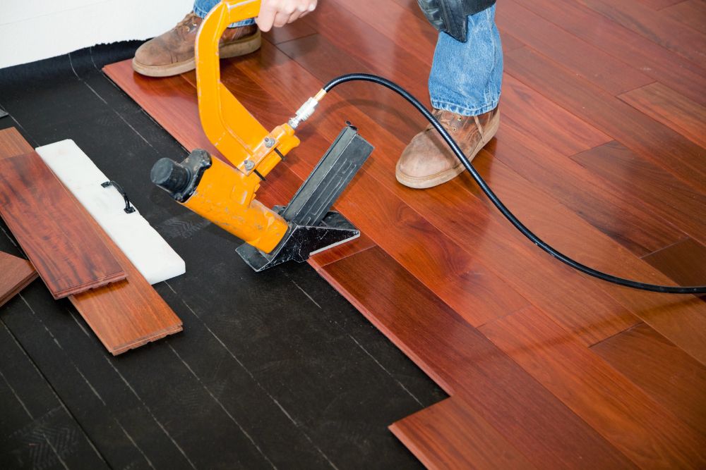 A man employs a nail gun to lay hardwood flooring, highlighting flooring services available in Renton, WA.