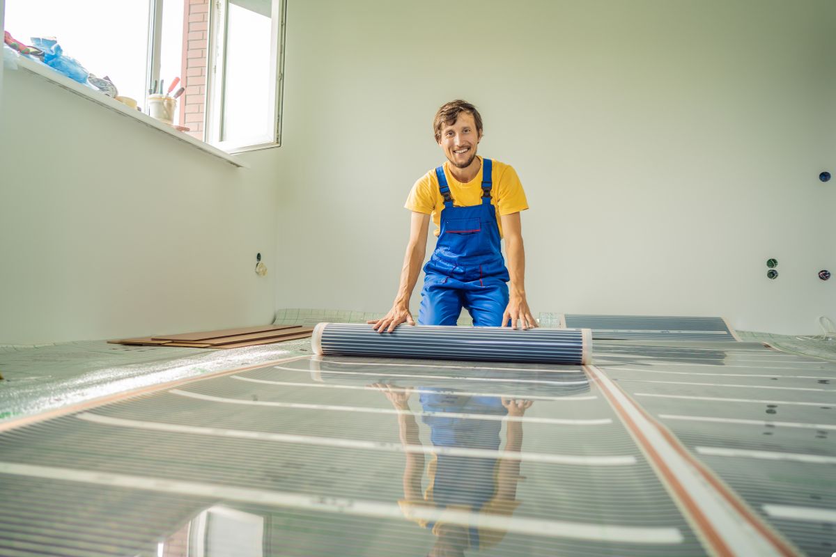 A man in overalls is positioned on the floor, with a roll of carpet beside him, indicating a flooring project.
