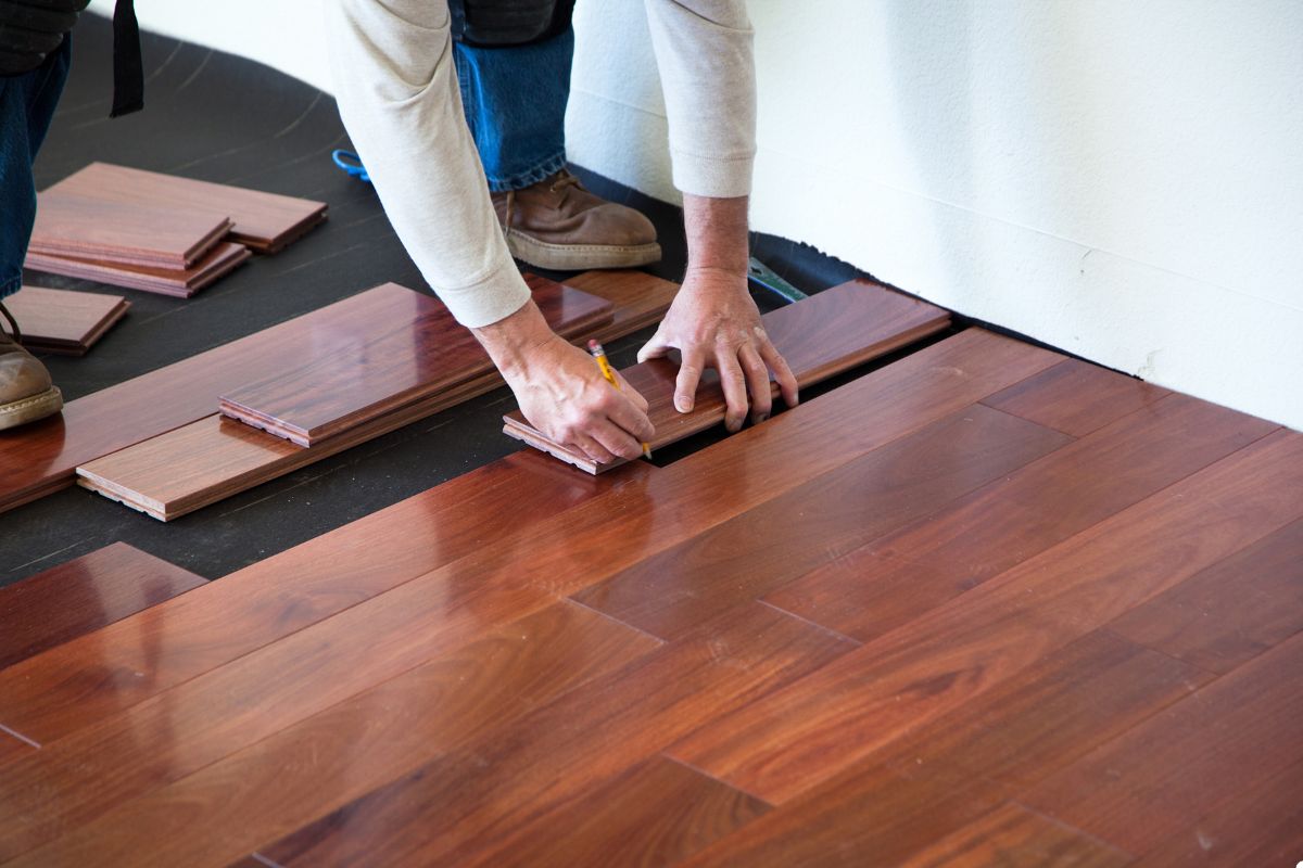 A man carefully installs wood flooring in a well-lit room, showcasing his craftsmanship and attention to detail.