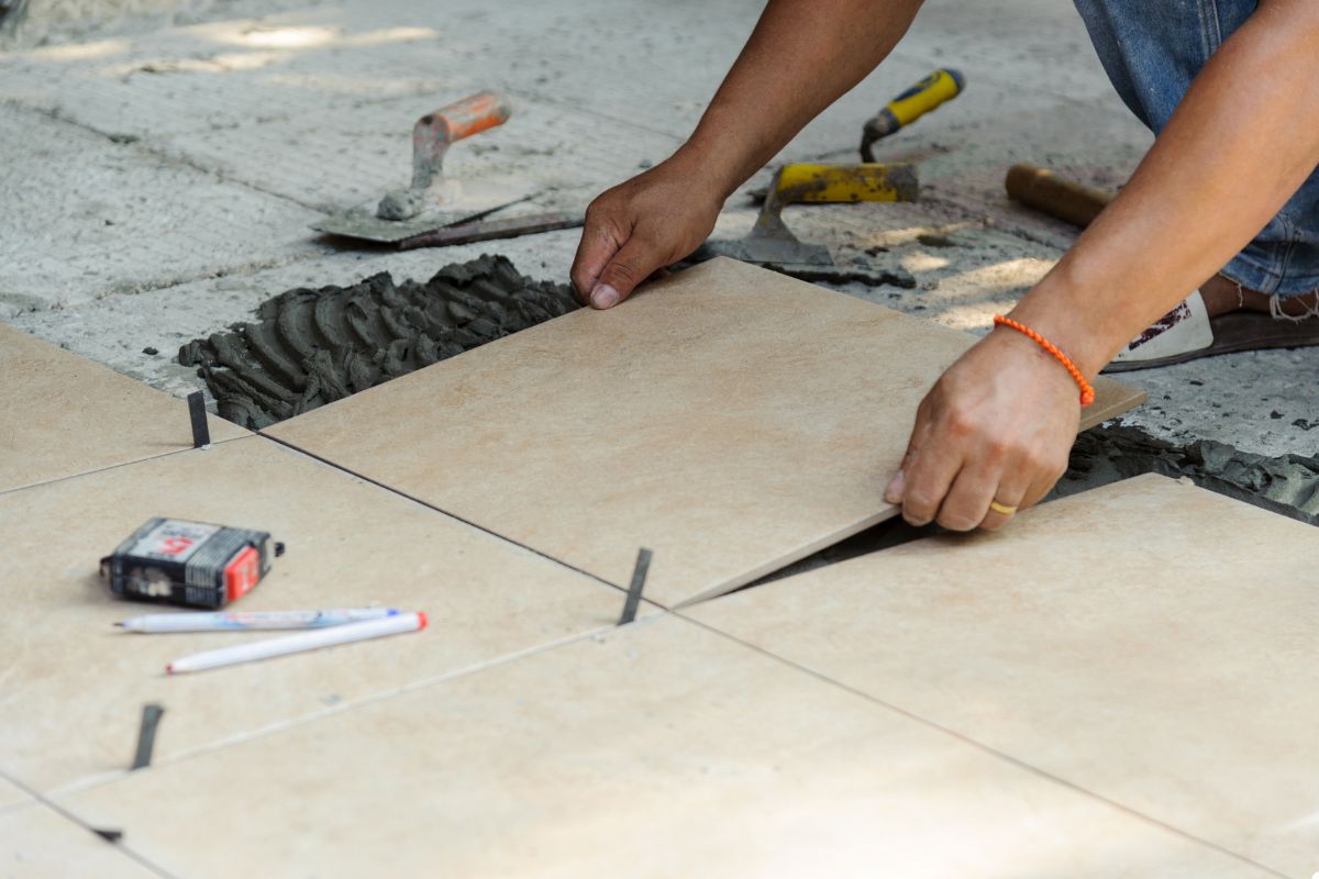 A man is engaged in the process of laying tiles on a floor, demonstrating skill and attention to detail. 