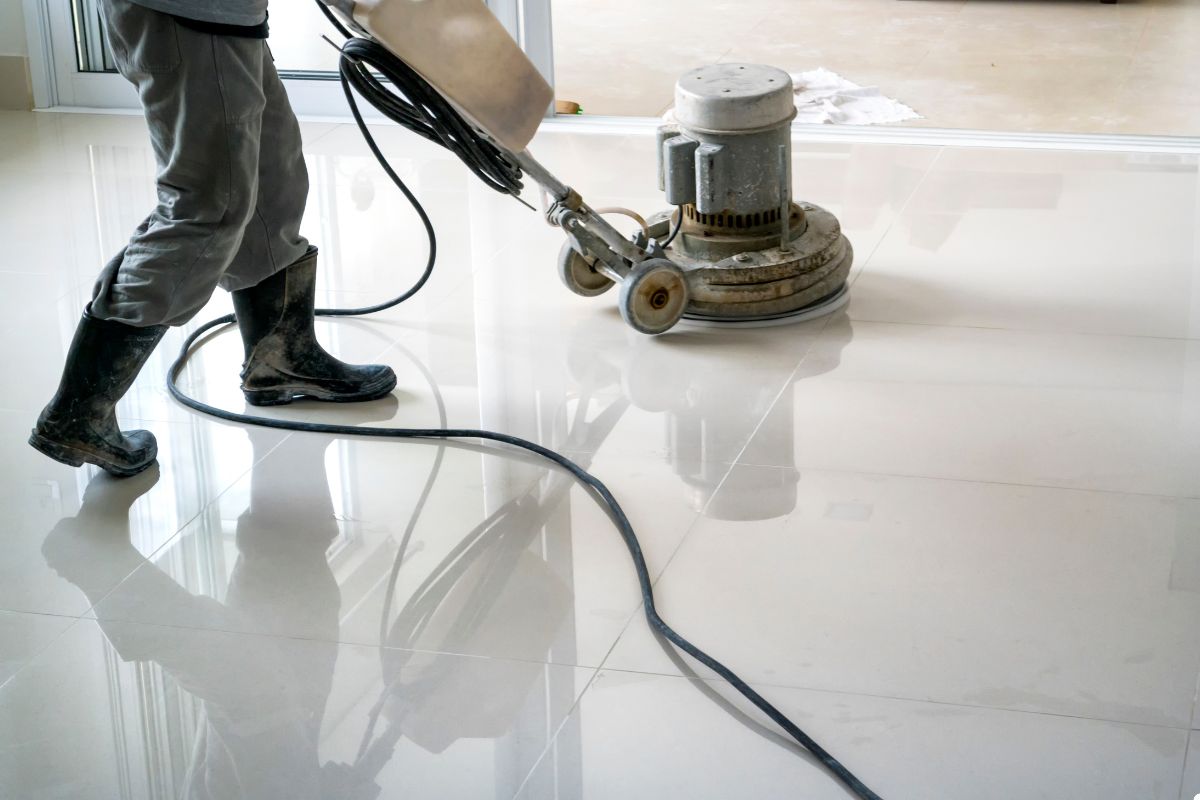 A man operates a vacuum cleaner on a pristine white tile floor, ensuring a thorough cleaning of the surface.